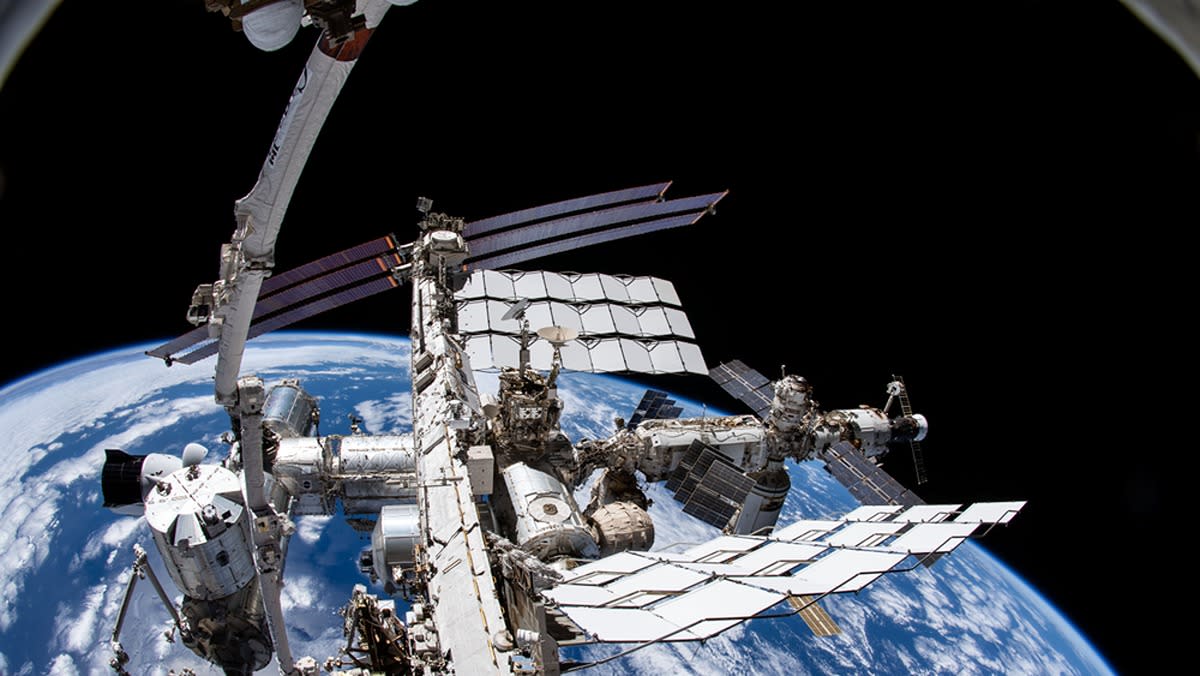  A fish eye lens view of the international space station with the canadarm extending up into black space. the earth is behind. 