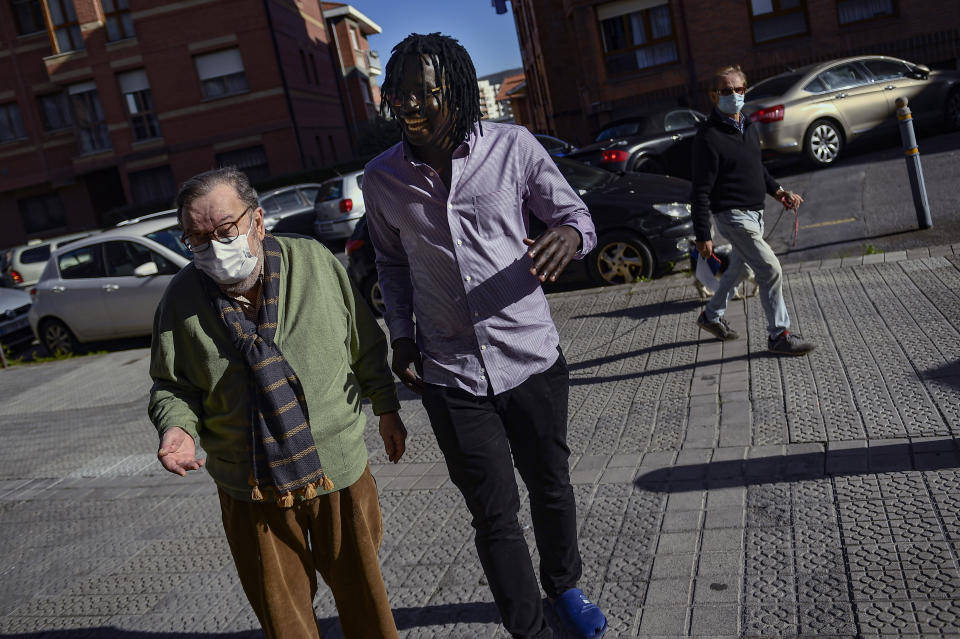 Mbaye Babacar Diouf, 33, centre, walks with his adoptive father Juan Gil, 74, in the basque city of Algorta, northern Spain, Wednesday, Nov. 18, 2020. Mbaye Babacar Diouf's life as a migrant in Europe took a turn for the better when he was adopted in Spain at the age of 28. That enabled him to pay his debts to human traffickers, study nursing and find a job at a Spanish hospital. Now he's giving back to the community. In a Bilbao hospital he cares for COVID-19 patients. (AP Photo/Alvaro Barrientos)