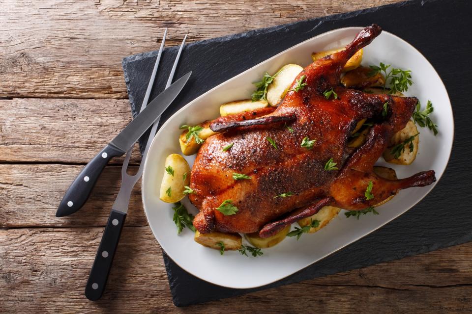 Roasted whole duck with apples on a platter and cutleries on the table.