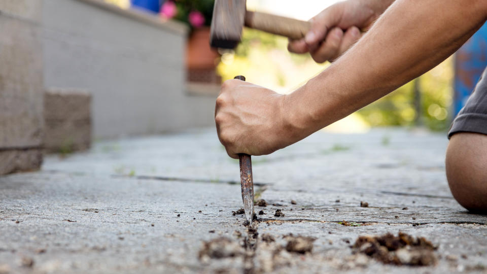 Someone removing old pointing from the patio with a hammer and chisel