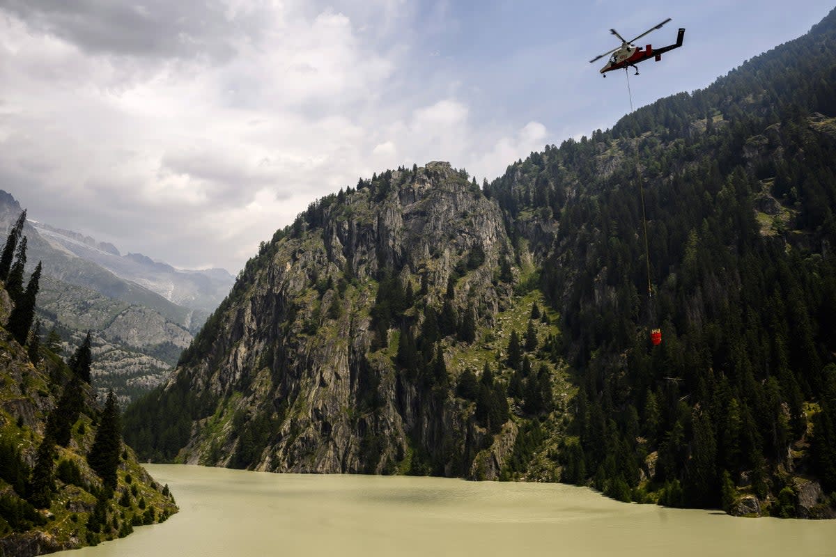 A helicopter refills its bucket over the Gibidum dam to extinguish the forest fire above the Switzerland communes of Bitsch and Ried-Moerel (EPA/Jean-Christophe Bott)