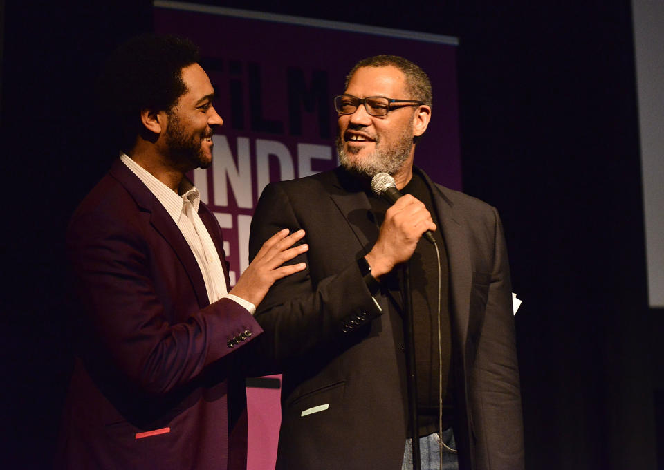 Langston onstage and smiling at his father, who's holding a microphone and smiling at him, as he touches his shoulder