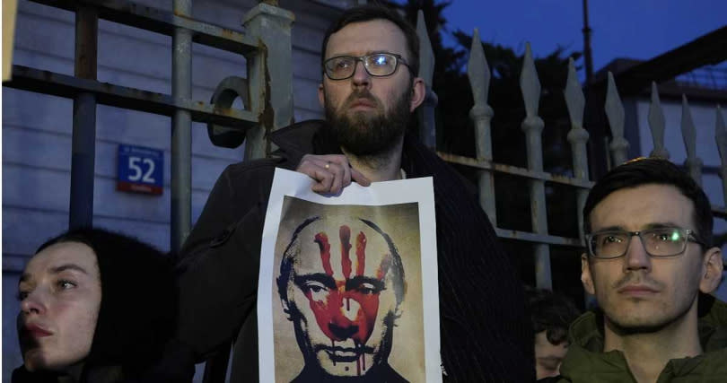 波蘭民眾在俄羅斯駐華沙的領事館前聚集，舉起一張蓋有血手印的普丁照片，諷刺普丁的雙手沾滿鮮血。（圖／達志／美聯社）