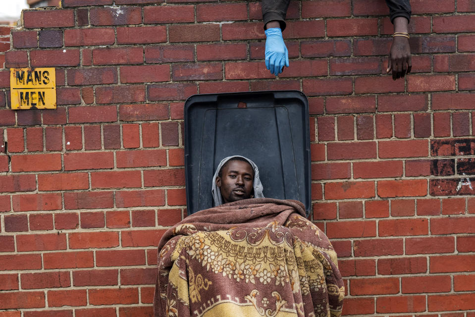 Henry sits in a bin as he and other homeless people rest at the Caledonian stadium downtown Pretoria, South Africa, Thursday April 2, 2020, after being rounded up by police in an effort to enforce a 21-day lockdown to control the spread of the coronavirus. Many of them being addicted, are receiving methadone syrup from a local NGO, and were complaining about the lack of sanitizer and soap. The new coronavirus causes mild or moderate symptoms for most people, but for some, especially older adults and people with existing health problems, it can cause more severe illness or death.(AP Photo/Jerome Delay)