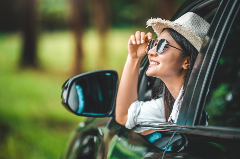 Happy woman hand holding hat outside open window car with meadow and mountain lake background. People lifestyle relaxing as traveler on road trip in holiday vacation. Transportation and travel concept