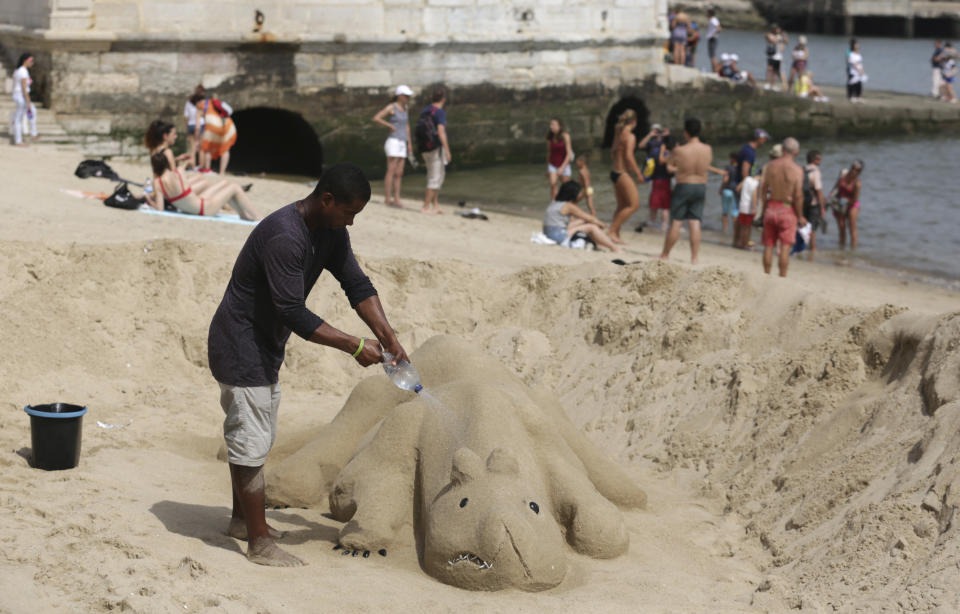 A man sprays water on his sand sculpture by the Tagus riverbank in Lisbon Thursday, Aug. 2 2018. The temperature in Lisbon reached 39 degrees Celsius, 102.2 Fahrenheit, on Thursday and is expected to keep rising over the next few days. (AP Photo/Armando Franca)