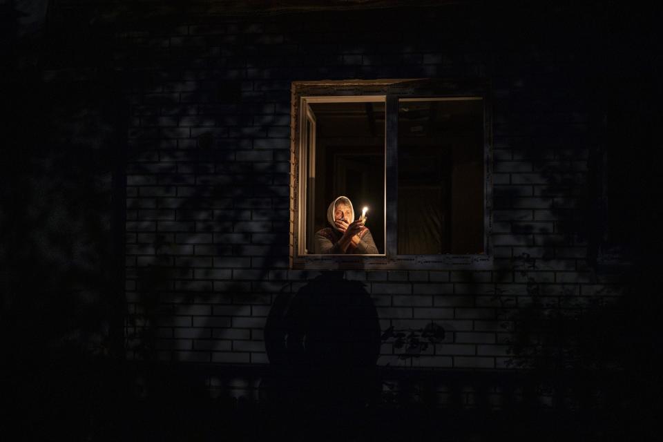 Catherine, 70, looks out the window while holding a candle for light inside her house during a power outage, in Borodyanka, Kyiv region, Ukraine, Thursday, Oct. 20, 2022. The image was part of a series of images by Associated Press photographers that was a finalist for the 2023 Pulitzer Prize for Feature Photography. (AP Photo/Emilio Morenatti)