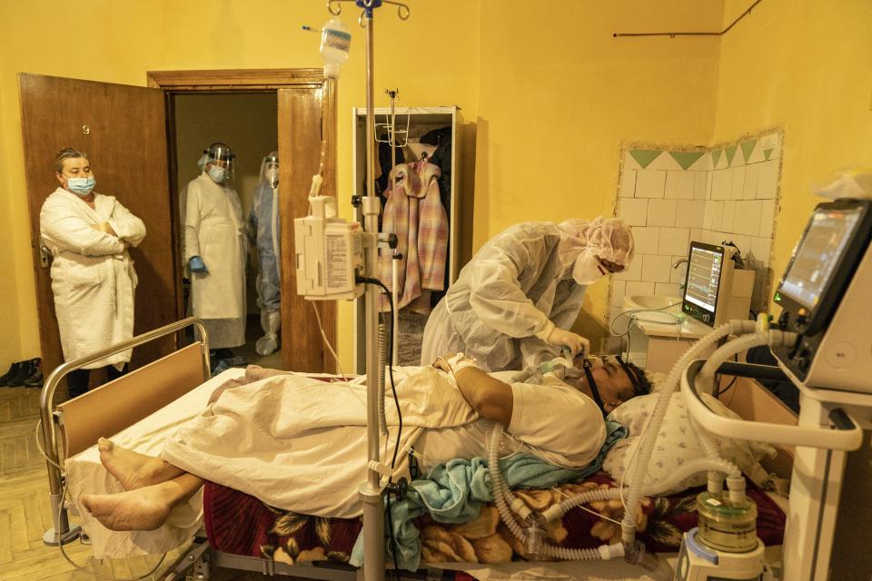 A medical worker treats Mykhailo Kaldarar, patient with COVID-19 as his wife Oleksandra Kaldarar, left, looks at him in a hospital in Rudky, Western Ukraine, on Tuesday, Jan. 5, 2021. Oleksandra Kaldarar shares the room with her husband, Mykhailo, and their son, who are both on ventilators. Ukraine imposed a broad lockdown Friday, but many medical workers in the country fear that it came too late and the long holidays, during which Ukrainians frequented entertainment venues, attended festive parties and crowded church services, will trigger a surge in new coronavirus infections. (AP Photo/Evgeniy Maloletka)