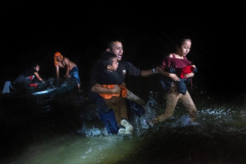 ROMA, TEXAS - APRIL 14: An immigrant father grips his children while walking ashore on the bank of the Rio Grande at the U.S.-Mexico border on April 14, 2021 in Roma, Texas. A smuggler (L), had rafted them over from Mexico with fellow immigrants. A surge of mostly Central American immigrants crossing into the United States, including record numbers of children, has challenged U.S. immigration agencies along the U.S. southern border. (Photo by John Moore/Getty Images)