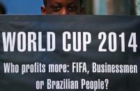 A boy holds up a banner as children sit at what is meant to represent a public school classroom, during a protest against the 2014 World Cup, organised by non-governmental organisation (NGO) Rio de Paz (Rio of Peace) at the Jacarezinho slum in Rio de Janeiro May 14, 2014. The protest was held to spread awareness about the need for the standard of Brazil's education system to be raised to that of its preparations for the World Cup, according to the organisation. REUTERS/Sergio Moraes (BRAZIL - Tags: SOCIETY SPORT SOCCER WORLD CUP EDUCATION CIVIL UNREST POVERTY)