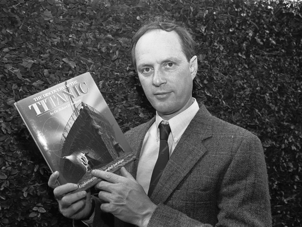 A black-and-white photo of Robert Ballard wearing a suit and tie, and holding his book titled “The Discovery of the Titanic.”