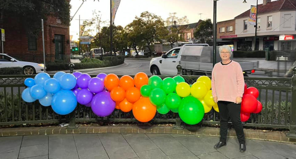 A woman stands in front of blue, purple, orange, green, yellow and red balloons to symbolise pride month and commemorate the LGBTQI+ community.