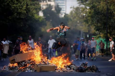 A man wearing roller blades jumps over a burning barricade during protests against Chile's government  - Credit: IVAN ALVARADO&nbsp;/Reuters