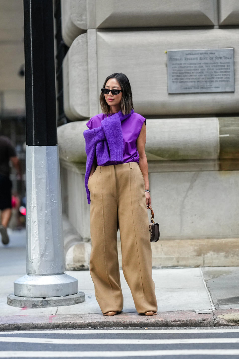 woman in purple tee, purple sweater, and brown pants.