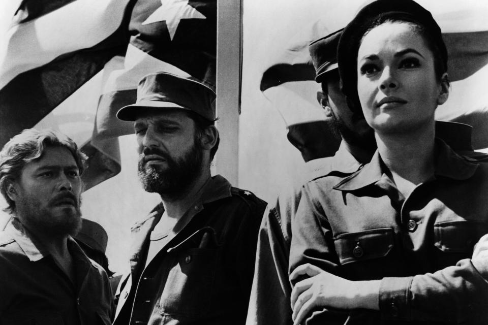 John Vernon and others in uniform stand before Cuban flag in a scene from the film 'Topaz', 1969. (Photo by Universal/Getty Images)