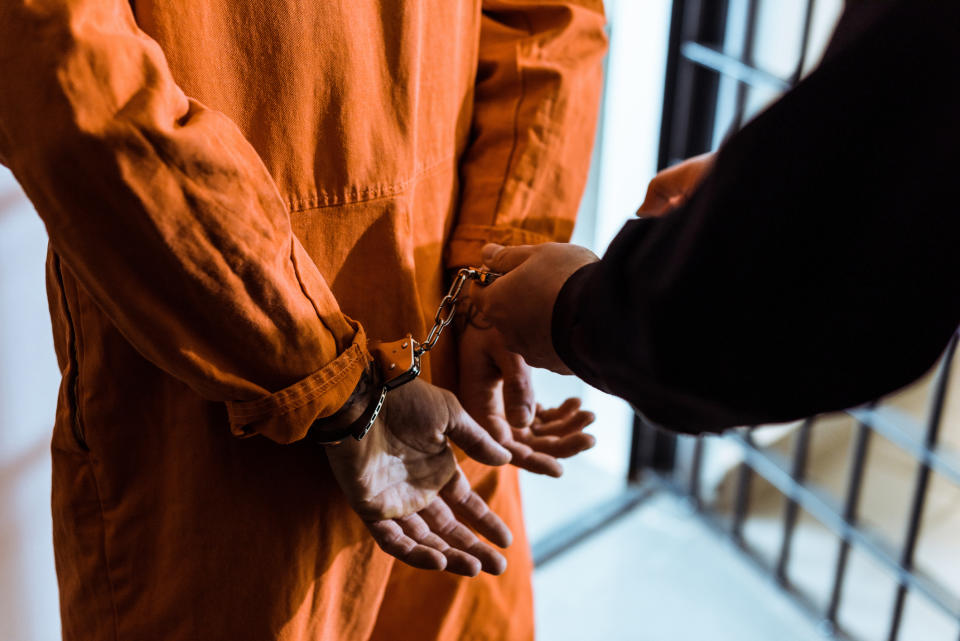 Person in orange jumpsuit being handcuffed by another individual, implying arrest or detention