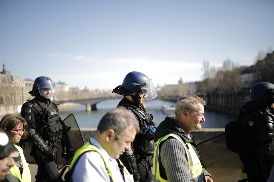 Yellow vest protesters are flanked by police riot officers as they demonstrate in the streets of Paris, France, Saturday, Feb. 23, 2019. French yellow vest protest organizers are trying to tamp down violence and anti-Semitism in the movement's ranks as they launch a 15th straight weekend of demonstrations. (AP Photo/Kamil Zihnioglu)