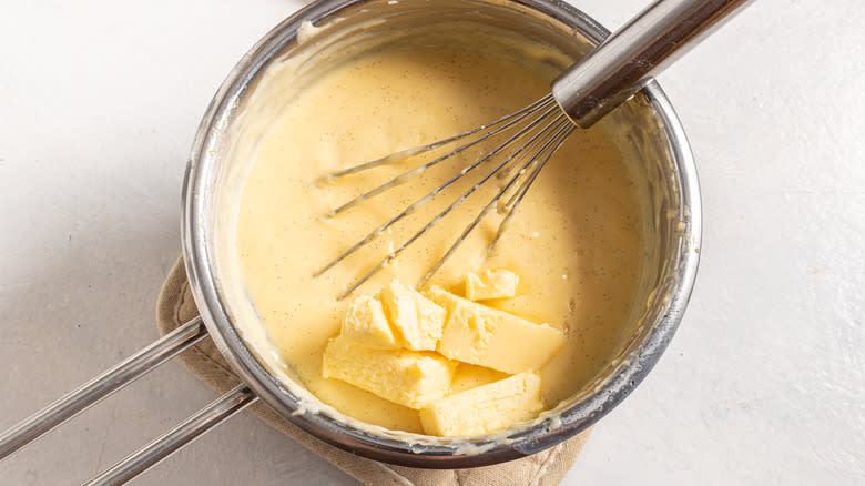 Saucepan with butter added to an egg custard with a whisk in it