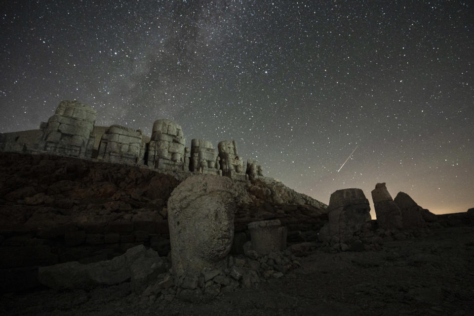 Starry night sky with several white streaks against stone structures.