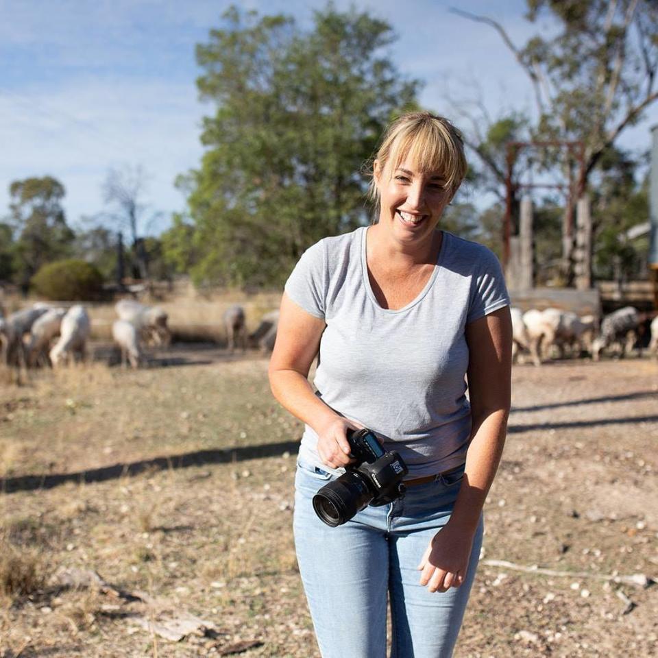 A smiling Chantel McAlister seen with camera in hand on a sheep farm. 