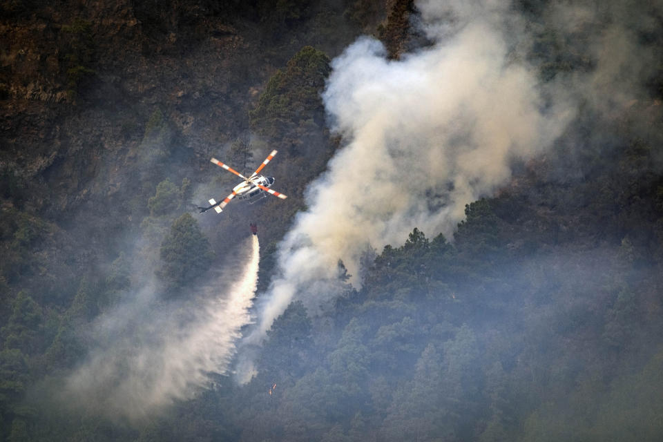 A helicopter drops water on the flames as the fire advances through the forest toward the town of Pinolere in Tenerife, Canary Islands, Spain on Saturday, Aug. 19, 2023. Thousands more residents of Tenerife in Spain's Canary Islands have fled their homes as a wildfire that authorities deemed "our of control" raged on for a fourth day. The regional government for the Canary Islands said that 4,000 more people were ordered to evacuate on Saturday. Those were in addition to the 4,500 people who on Friday were forced to move out of danger's way. (AP Photo/Arturo Rodriguez)