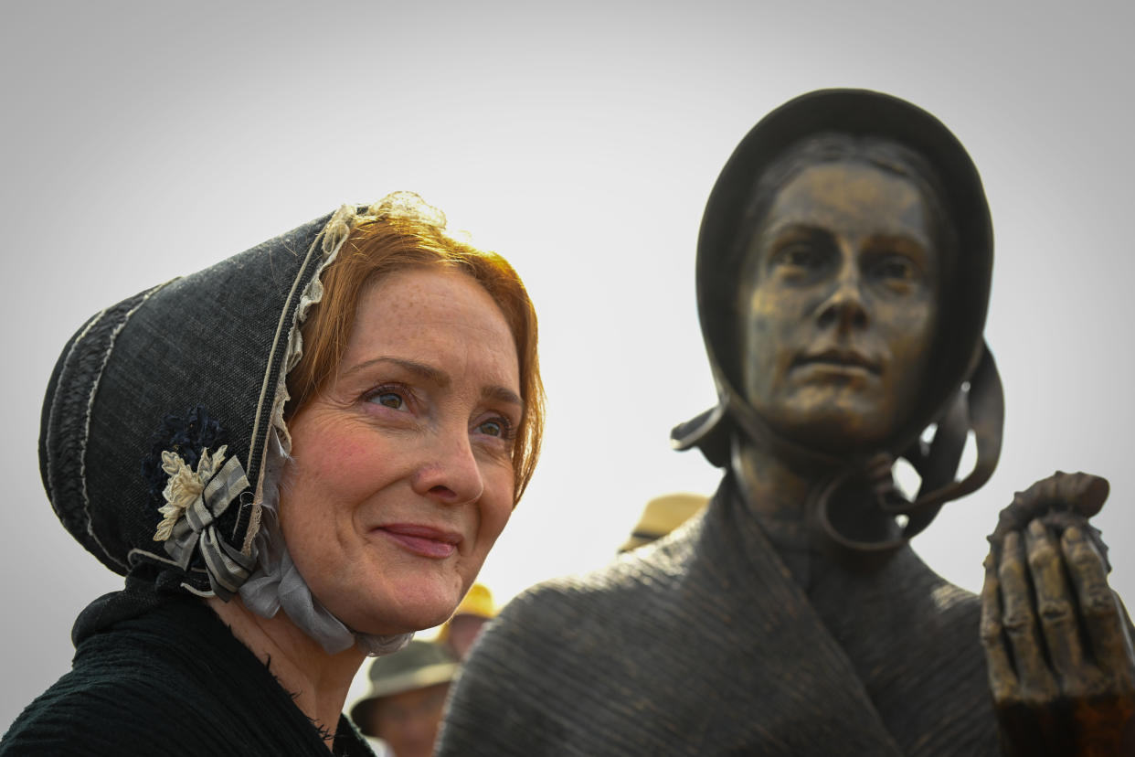 Una mujer vestida como Mary Anning posa junto a su estatua desvelada el 21 de mayo de 2022 en Lyme Regis, Inglaterra. (Photo by Finnbarr Webster/Getty Images)