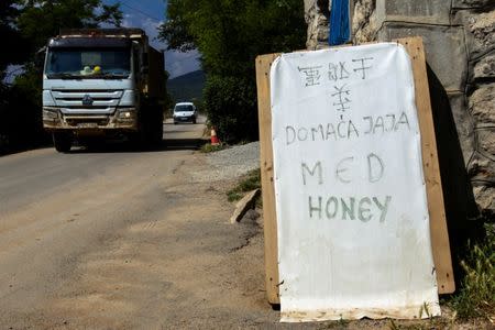 Construction trucks pass by a board advertising homemade eggs and honey in Chinese, Montenegrin and English on the Bar-Boljare highway construction site in the village of Pelev Brijeg, Montenegro June 11, 2018. Picture taken June 11, 2018. REUTERS/Stevo Vasiljevic