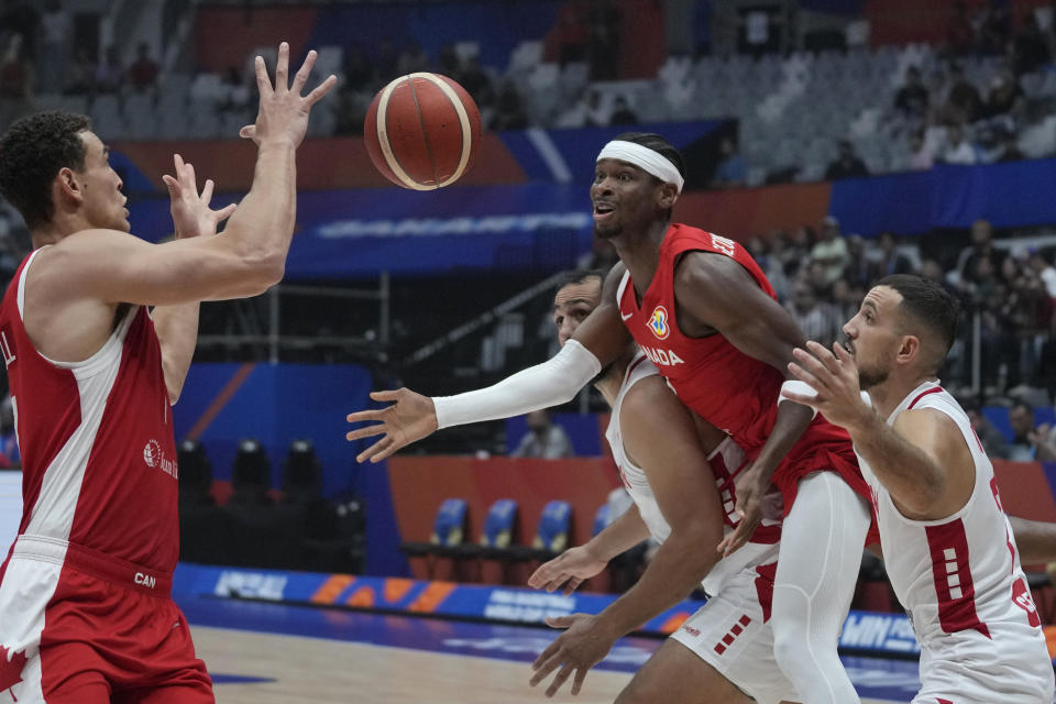 Canada guard Shai Gilgeous-Alexander passes the ball to teammate Dwight Powell as Lebanon guard Ali Mezher, right, and forward Ali Haidar, third right, react during the Basketball World Cup group H match between Canada and Lebanon at the Indonesia Arena stadium in Jakarta, Indonesia, Sunday, Aug. 27, 2023. (AP Photo/Dita Alangkara)