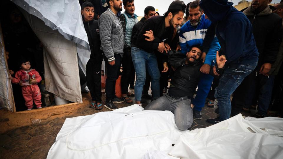 PHOTO: Displaced Palestinian children watch from inside a tent as a man mourns relatives, who were killed in an overnight Israeli airstrike on the Al-Maghazi refugee camp, during a mass funeral in Deir al-Balah in the central Gaza Strip on Dec. 25, 2023. (Mahmud Hams/AFP via Getty Images)