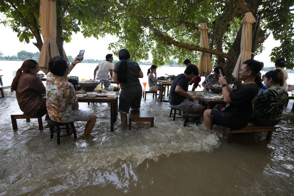 Customers of the riverside Chaopraya Antique Café react to a passing boat's wake as they enjoy themselves in the extraordinary high water levels in the Chao Phraya River in Nonthaburi, near Bangkok, Thailand, Thursday, Oct. 7, 2021. The flood-hit restaurant has become an unlikely dining hotspot after fun-loving foodies began flocking to its water-logged deck to eat amid the lapping tide. Now, instead of empty chairs and vacant tables, the cafe is as full as ever, offering an experience the canny owner has re-branded as “hot-pot surfing.” (AP Photo/Sakchai Lalit)