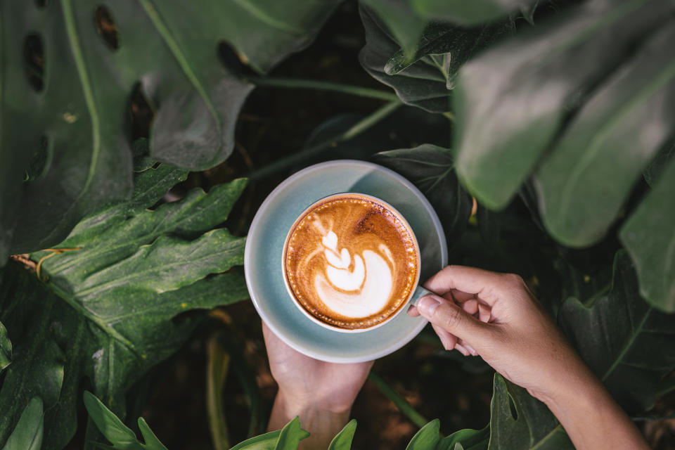 Asian woman hand holding cups of hot coffee latte in the garden