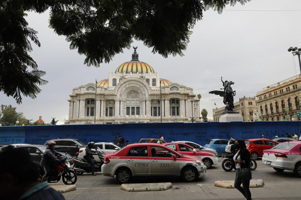 Pedestrians and cars pass in front of the Palace of Fine Arts amidst the "new normal" of the ongoing coronavirus pandemic, in central Mexico City, Monday, Aug. 10, 2020. (AP Photo/Rebecca Blackwell)