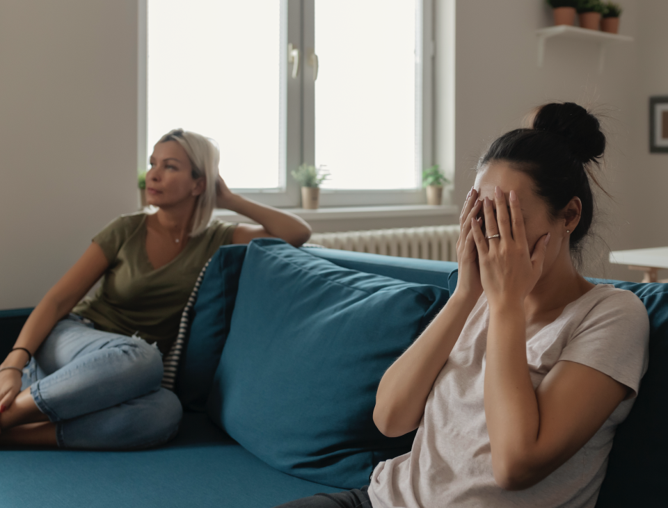 Two people sitting, one with hands covering face showing distress, the other looking on with concern