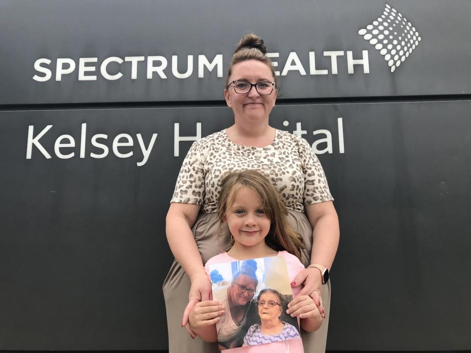 Samantha Wright, of Cato Township, stands with her daughter, Kinsleigh, 6, who holds a photo of Wright and Wright's mother, Brenda Glasspoole, outside Corewell Health's Spectrum Health Kelsey Hospital in Lakeview, Mich., on Aug. 24, 2023. Glasspoole was a long-term care resident who was moved to hospice care in Reed City an hour away because the hospital in Lakeview is being shuttered.