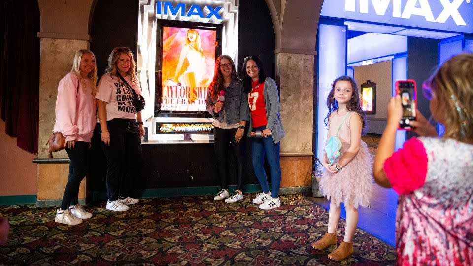 A young Taylor Swift fan takes a photo of the moms of their group next to the "Taylor Swift: The Eras Tour" poster before they go in to see the movie at Malco Paradiso Cinema Grill and IMAX in Memphis, Tenn., on Saturday, October 14, 2023. - Chris Day/The Commercial Appeal/USA Today Network