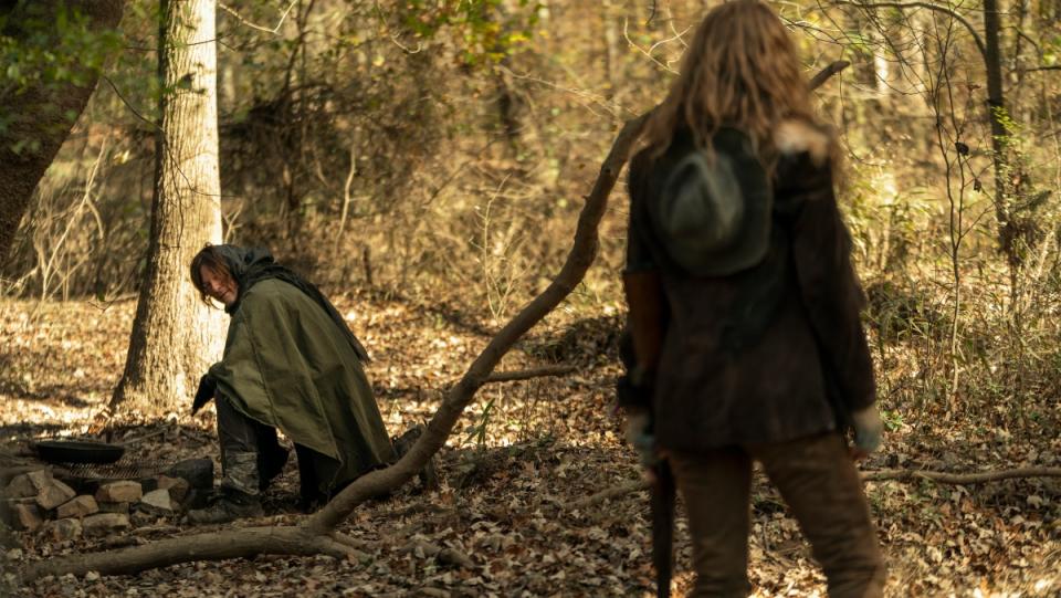 a photo of a woman facing away from the camera wearing a brown coat and pants towards a man facing the camera in the woods on the walking dead Daryl Dixon 