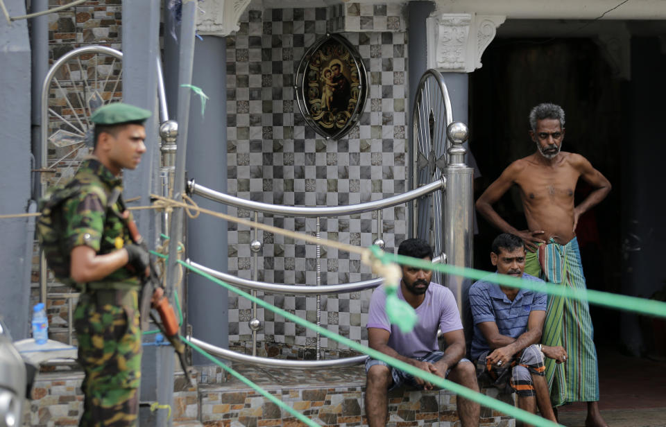 A Sri Lankan police commando secure the area of the exploded St. Anthony's Church on Easter Sunday attacks as people wait next to a small roadside in Colombo, Sri Lanka, Sunday, April 28, 2019. Sri Lanka's Catholics on Sunday awoke preparing to celebrate Mass in their homes by a televised broadcast as churches across the island shut over fears of militant attacks, a week after the Islamic State-claimed Easter suicide bombings. (AP Photo/Eranga Jayawardena)