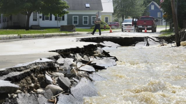 A passer-by walks near a street damaged by flood waters.