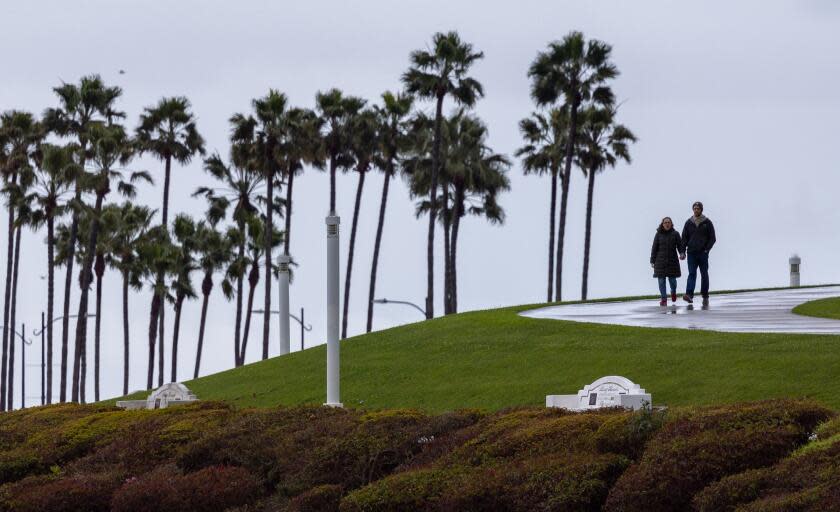 Long Beach, CA - March 06: A couple hold hands as they walk amid light rain at ShoreLine Aquatic Park in Long Beach Wednesday, March 6, 2024. (Allen J. Schaben / Los Angeles Times)