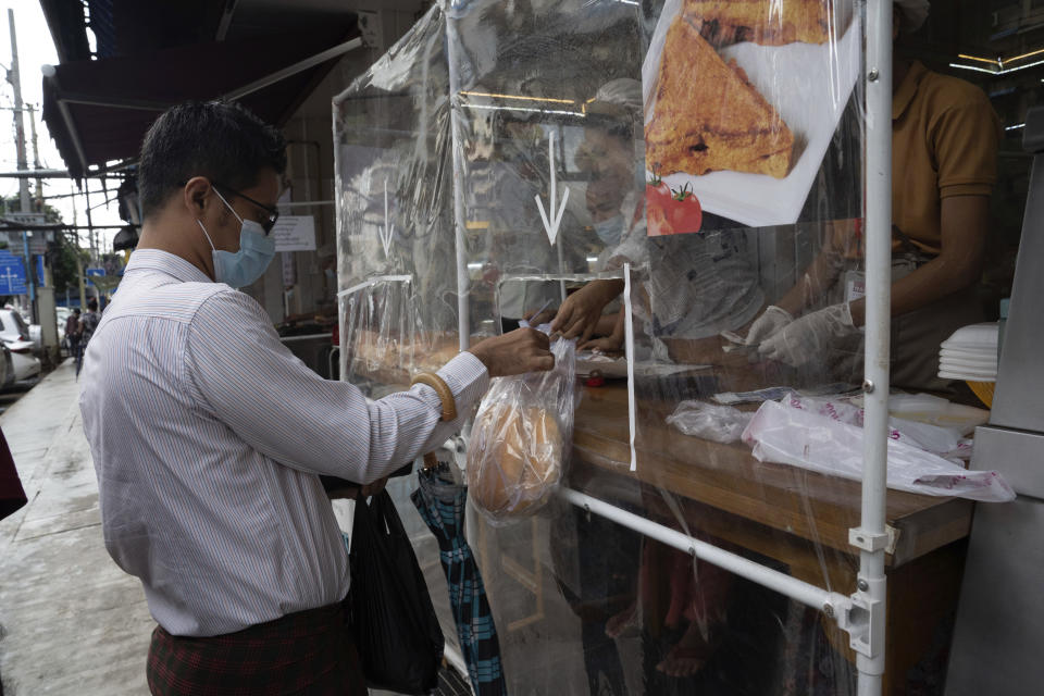 A man wearing a face mask receives take-away food handed over from behind a plastic sheet at a restaurant in Yangon, Myanmar,Monday, Sept. 21, 2020. Myanmar, faced with a rapidly rising number of coronavirus cases and deaths, has imposed the tightest restrictions so far to fight the spread of the disease in Yangon, the country's biggest city and main transportation hub. (AP Photo/Pyae Sone Win)