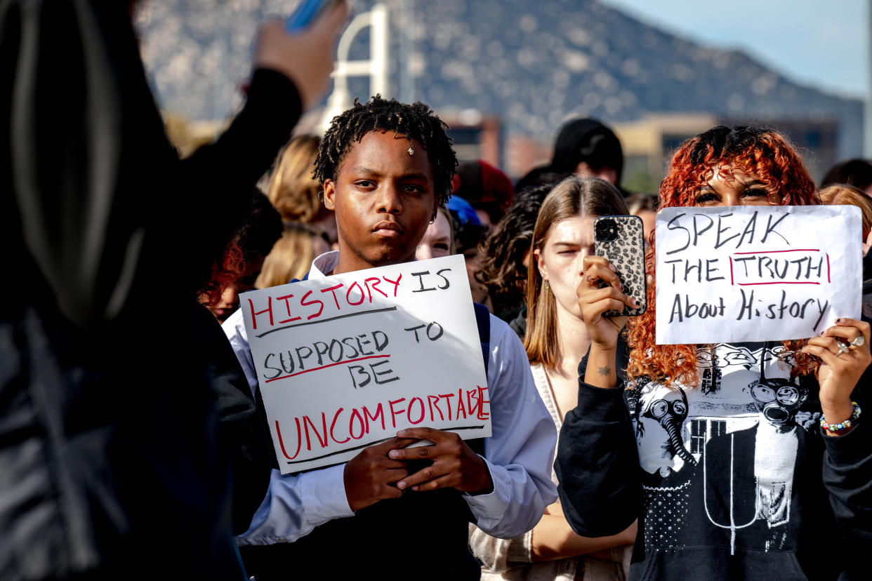 High school students hold signs reading: History is supposed to be uncomfortable.