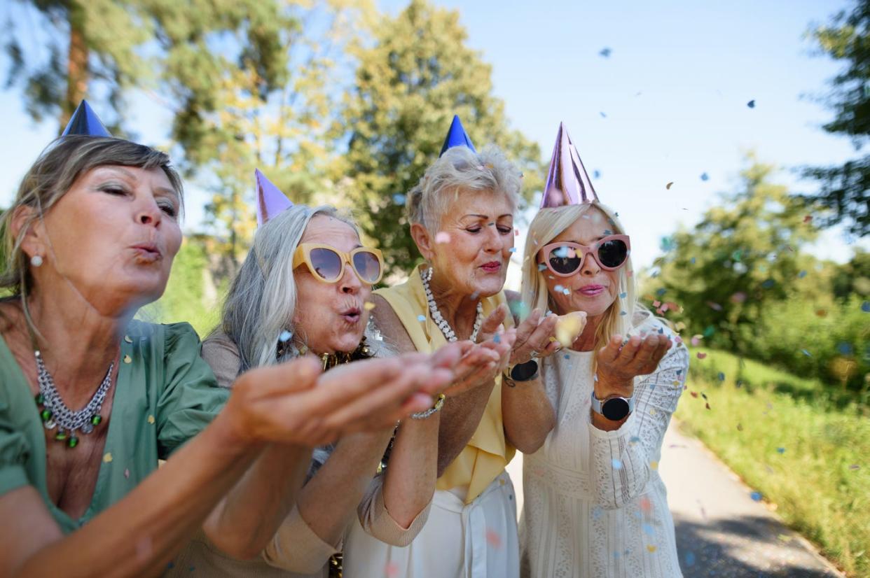 senior female friends in party hats blowing confetti