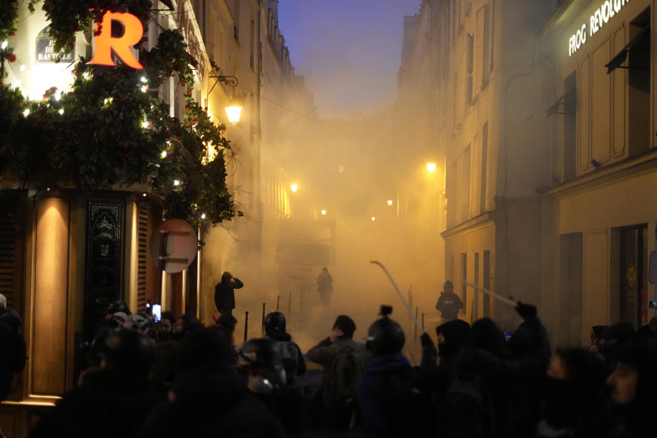 Youths face riot police officers, background, during scuffles as part of a demonstration against plans to push back France's retirement age, Tuesday, Feb. 7, 2023 in Paris. The demonstration comes a day after French lawmakers began debating a pension bill that would raise the minimum retirement from 62 to 64. The bill is the flagship legislation of President Emmanuel Macron's second term. (AP Photo/Thibault Camus)