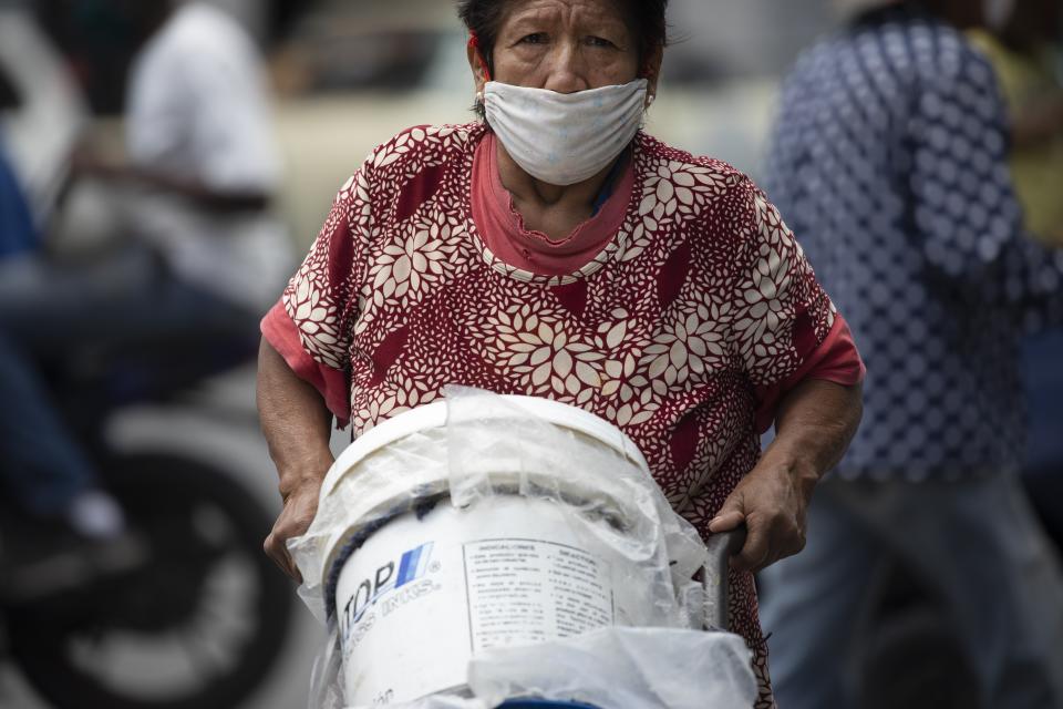 A woman, wearing a protective face mask, pushes a dolly of containers filled with water, in Caracas, Venezuela, Saturday, June 20, 2020. An estimated 86% of Venezuelans reported unreliable water service, including 11% who have none at all, according to an April survey by the non-profit Venezuelan Observatory of Public Services. (AP Photo/Ariana Cubillos)