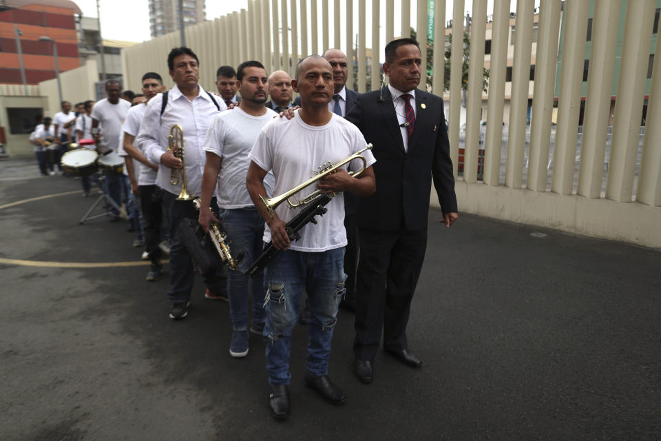 In this July 19, 2019 photo, accompanied by prison guards, inmates stand in a line holding their instruments, after arriving at the national theater in Lima, Peru, to take part in a classical music session with the symphony orchestra. Nearly 50 guards kept a close eye on the prisoners during the music class before escorting them back to El Callao, their coastal prison in Lima. (AP Photo/Martin Mejia)