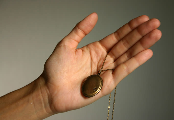 A hand holds an antique round locket attached to a chain