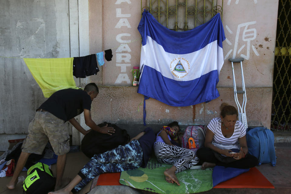 In this Oct. 23, 2018 photo, Nicaraguan Lester Javier Velasquez Gonzalez, left, his 14-year-old son Axel, 9-year-old daughter Alexa Michelle and wife Idania Molina Rocha, rest on a sidewalk beneath a Nicaraguan national they proudly hung on the wall, while travelling with a migrant caravan to the U.S., in Huixtla, Mexico. While most people joined spontaneously as word of the caravan spread, their long, terrible journey began in early July when the Nicaraguan government launched a crackdown on opposition protests demanding President Daniel Ortega leave office. (AP Photo/Moises Castillo)