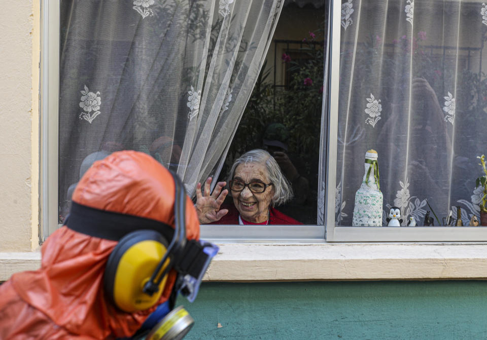 A woman waves to a city worker dressed in a hazmat suit as he disinfects the streets in her neighborhood as a precaution against the spread of the new coronavirus, in Santiago, Chile, April 15, 2020. (AP Photo/Esteban Felix)