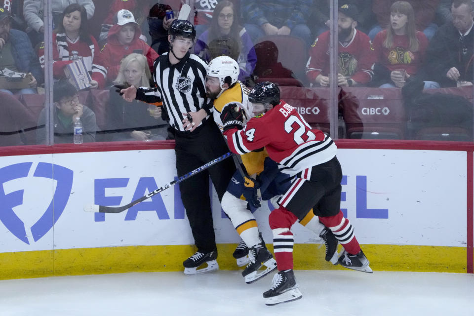 Chicago Blackhawks' Anders Bjork (24) checks Nashville Predators' Dante Fabbro, center, into the boards and referee Justin Kea, left, during the second period of an NHL hockey game Saturday, March 4, 2023, in Chicago. (AP Photo/Charles Rex Arbogast)