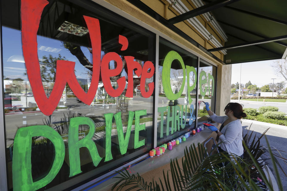 Lucy Kwak paints a sign on the window of a fast food chain's restaurant indicating that the drive-thru window is still open as well as a takeout optionduring the coronavirus outbreak in Garden Grove, Calif., Thursday, March 26, 2020. (AP Photo/Chris Carlson)